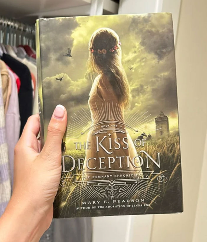 Hand holding "The Kiss of Deception" book, an alternative to Rebecca Yarros' "Onyx Storm".