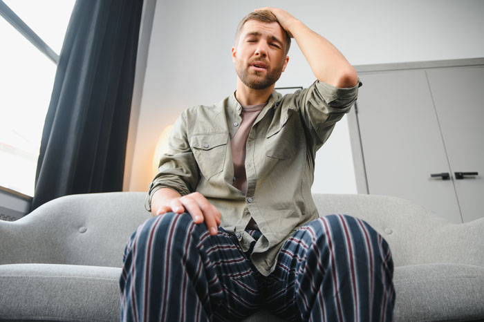 Man sitting on a couch, looking frustrated, wearing a green shirt and striped pants, reflecting on novel planning incident.