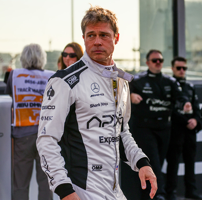 Actor in racing suit at motorsport event, showcasing tattoos.