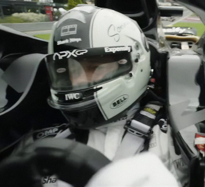 Race car driver in helmet and suit, focused in the cockpit, Brad Pitt tattoos unseen.