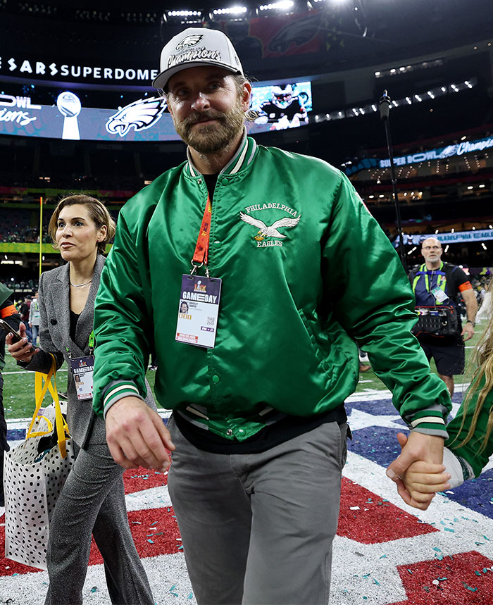 Man in green Eagles jacket and hat at Super Bowl 2025, holding hands on the field.