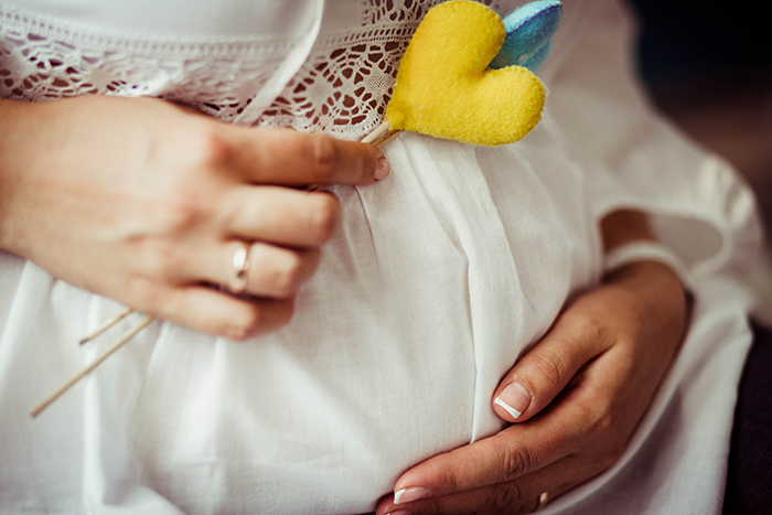 Pregnant bride in white dress, holding a yellow felt heart on her belly. Pregnant bride in white dress, holding a yellow felt heart on her belly.
