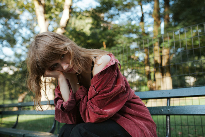 A woman in a red sweater looking pensive, sitting on a park bench.