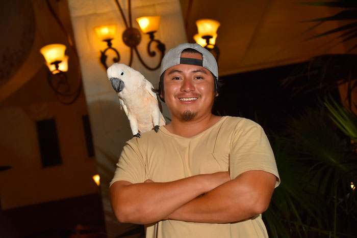 Man smiling with a parrot on his shoulder, indoor lighting, addressing pet parenting.