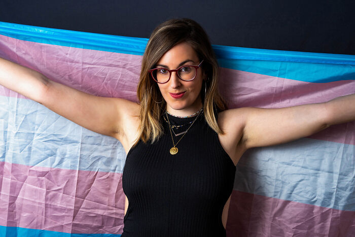 Person in glasses holding a striped flag, expressing love and pride.