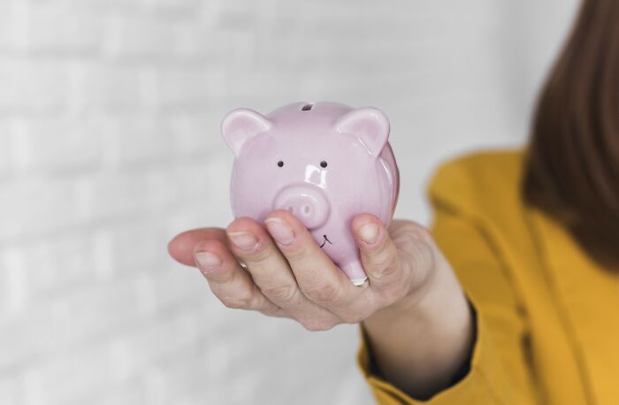 A person holding a pink piggy bank in their hand, symbolizing advice from father on saving money.