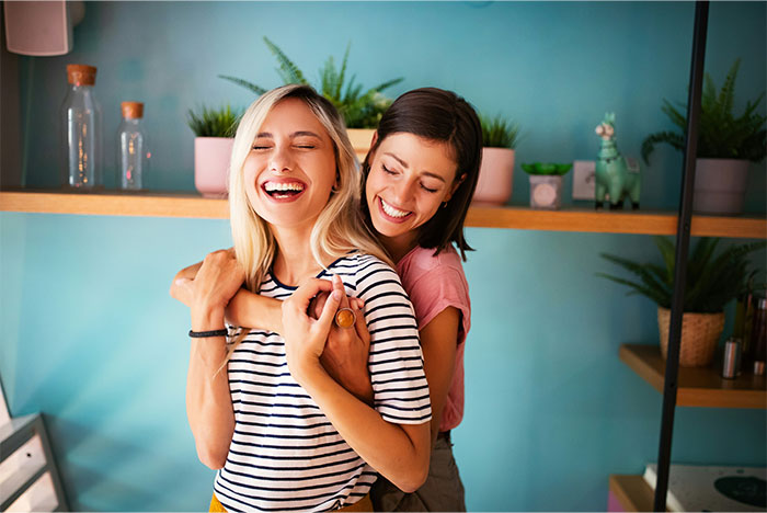 Two women smiling in a cozy room, reflecting joy and togetherness amidst plants and home decor. Two women smiling in a cozy room, reflecting joy and togetherness amidst plants and home decor.