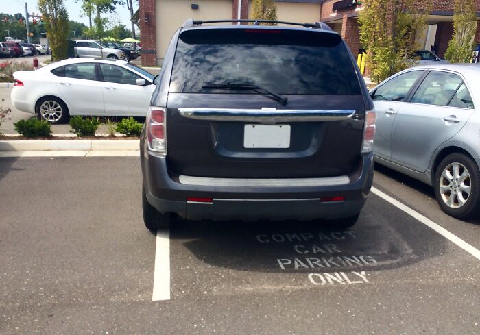 Black SUV parked across two compact car spaces in a parking lot creating an insane workplace moment.