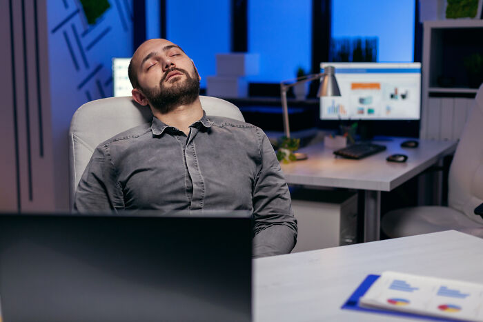 Man sleeping at desk late at night in office, one of the insane workplace moments captured in a modern workspace.