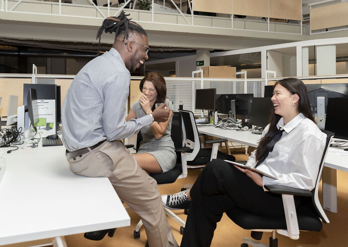 Three diverse coworkers sharing a laugh during an informal meeting, capturing insane workplace moments and teamwork.