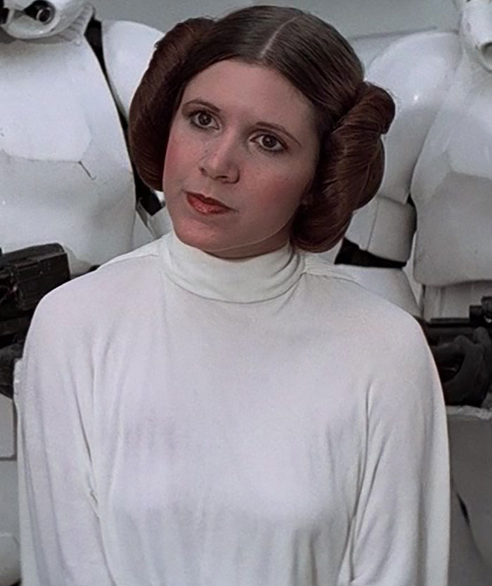 Actress in iconic sci-fi role, wearing a white gown and surrounded by stormtroopers. Celebrities tragically passed away.