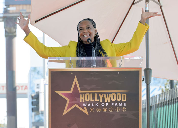 Margaret Avery at Hollywood Walk of Fame ceremony, speaking with arms raised, representing Netflix hit series cast.