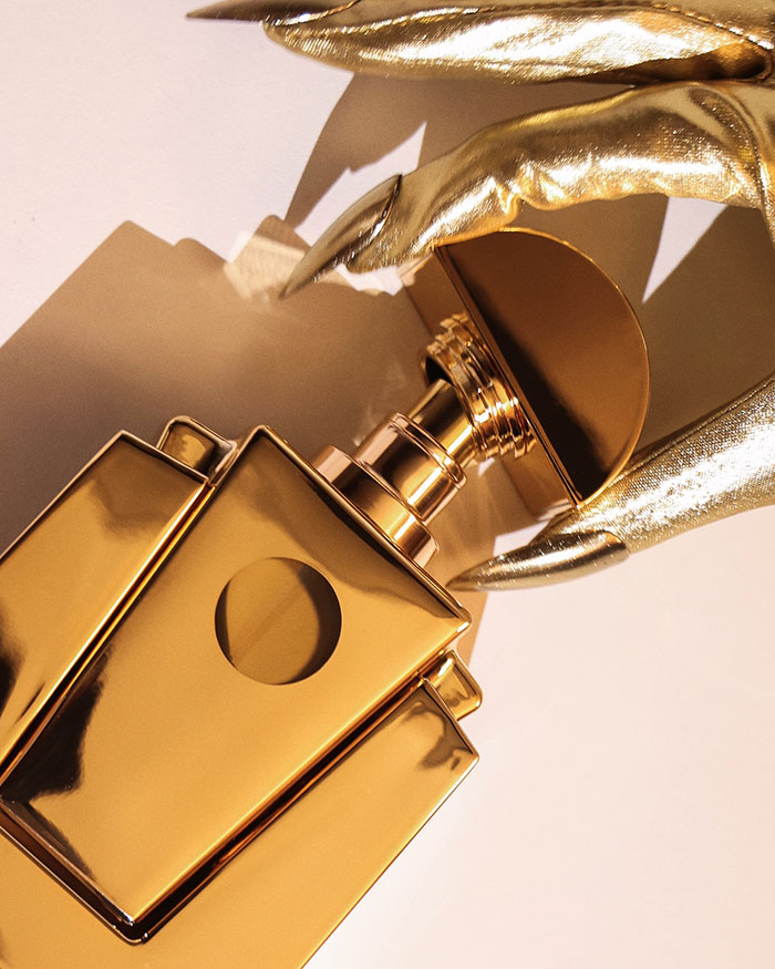 Golden Ce Lumiere perfume bottle with gold-gloved hand, reflecting elegant luxury and style.