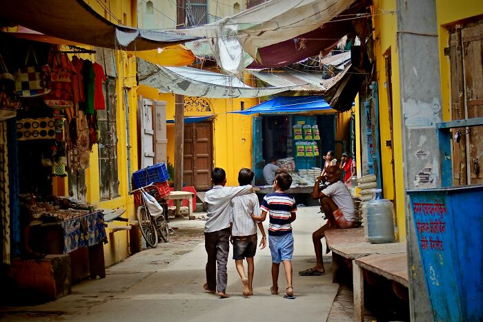 Children walking down a vibrant, busy alleyway, experiencing a cultural setting in another country.