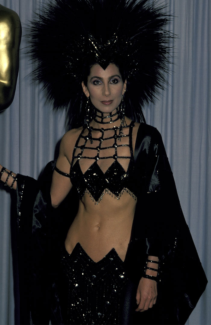 Celebrity in an elaborate black outfit with a striking headdress, showcasing bold fashion.