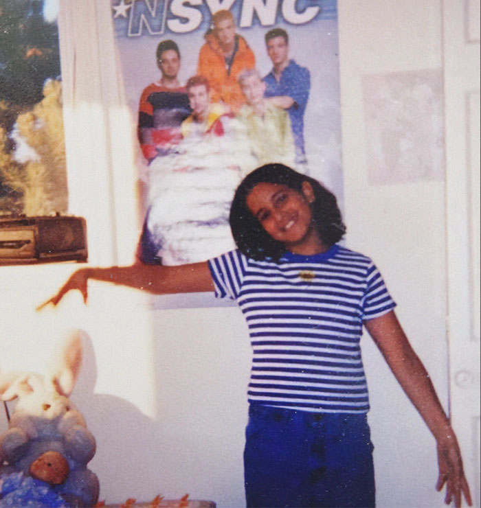 Young woman in a striped shirt smiling in a room with an NSYNC poster, related to a Mormon family adoption story.