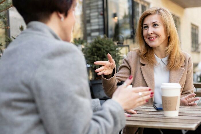Two women engaged in conversation at an outdoor café, discussing common USA things over coffee.