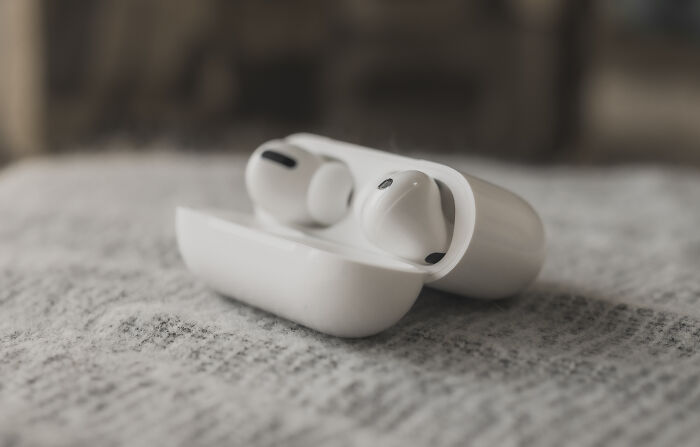 Wireless earbuds in a case on a textured surface, emphasizing common hygiene habits to prevent stinky buildup.