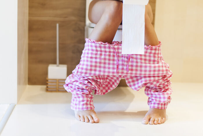 Person wearing pink checkered pants sitting on a toilet, emphasizing travel essentials for comfort.