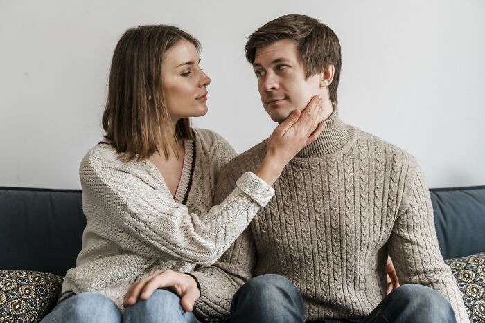 A couple sitting on a sofa, a woman gently touches a man's face, illustrating expressions of love and affection.