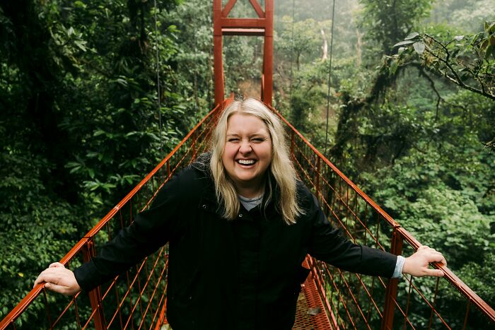Smiling woman on a red bridge surrounded by lush greenery.