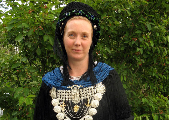 Person in traditional attire with intricate embroidery in front of leafy green background, showcasing cultural myth beliefs.