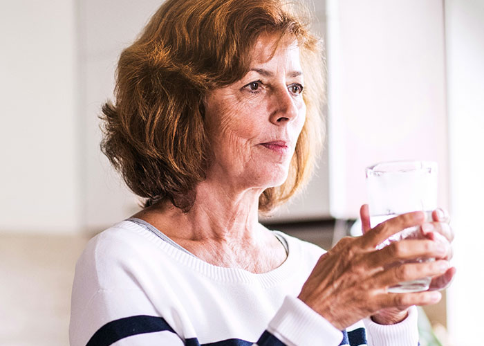 Mujer madura con rasgos poco convencionales sosteniendo un vaso de agua, mostrando belleza única y poco atractiva.