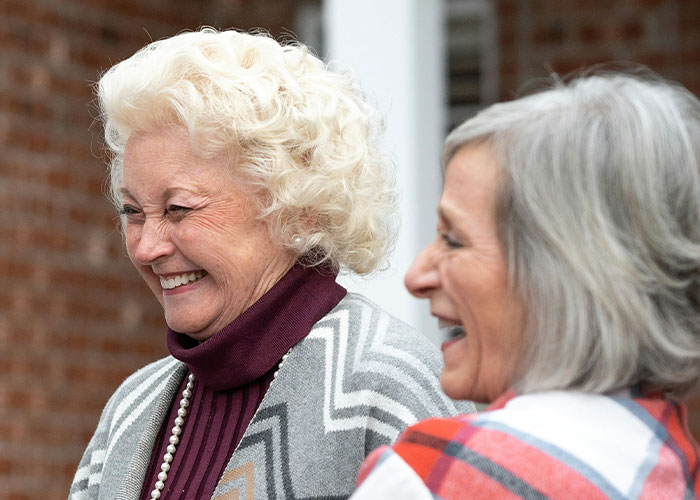 Dos mujeres mayores sonriendo y disfrutando juntas, destacando rasgos poco atractivos que resultan encantadores para ellas.