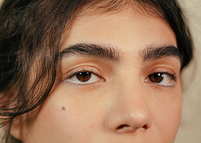 Primer plano de rostro con rasgos poco atractivos vistos como atractivos, destacando cejas pobladas y lunar en la mejilla.