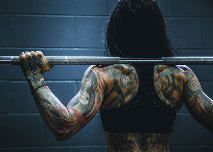 Mujer tatuada levantando pesas, mostrando rasgos considerados poco atractivos pero atractivos para algunas personas.