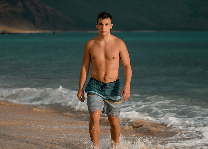 Hombre caminando en la playa con rasgos considerados poco atractivos pero vistos como atractivos por algunos.