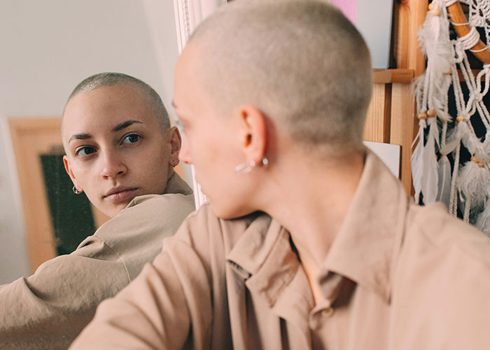 Persona con rasgos poco atractivos reflejada en espejo, mostrando confianza y estilo único en un entorno moderno.