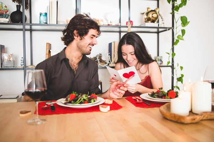 Couple enjoying a romantic dinner, sharing a simple and adorable Valentine's gift card with heart design.