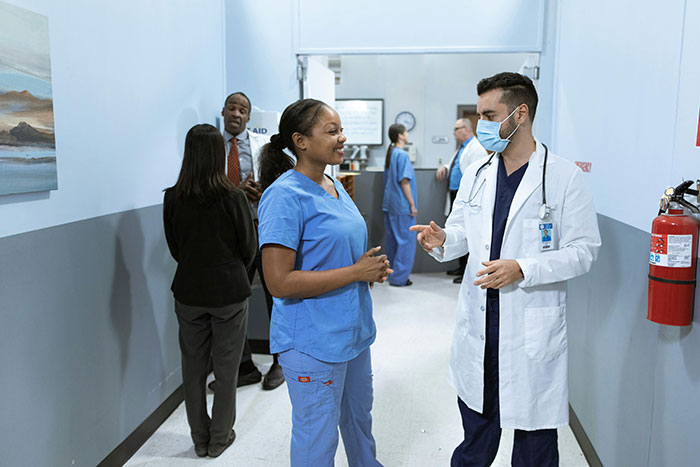 Doctor converses with nurse in hospital corridor, highlighting coworker dynamics. Doctor converses with nurse in hospital corridor, highlighting coworker dynamics.