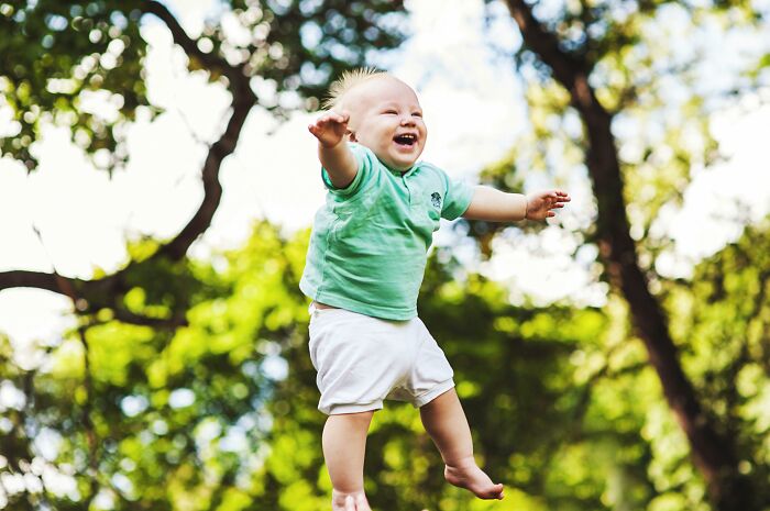 A joyful child in a green shirt being tossed in the air, surrounded by lush green trees.