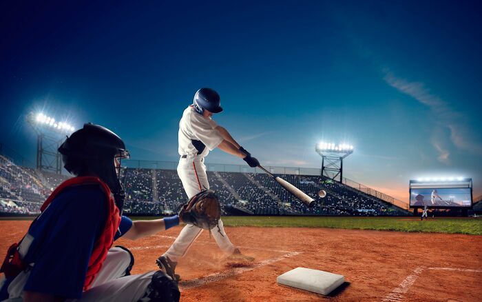 Baseball player swinging bat under stadium lights, with catcher ready to catch the ball, represents stories of trauma.