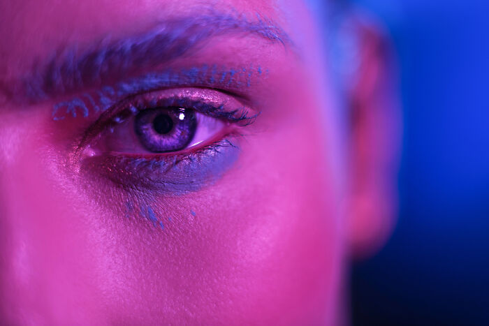 Close-up of a person's eye illuminated with pink and blue light, conveying a haunting and eerie atmosphere.