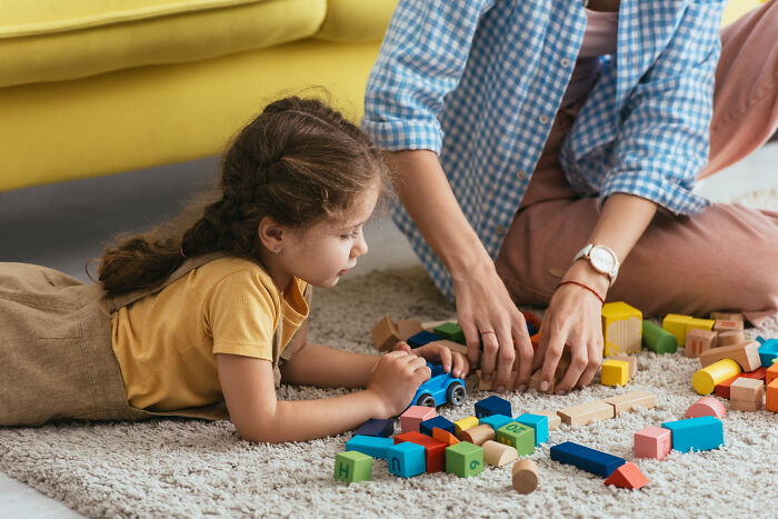 Child playing with colorful blocks on a carpet, engaged in creative activity.