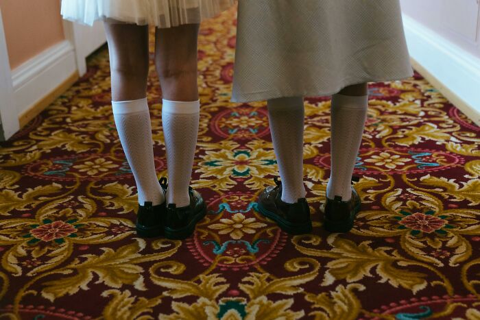 Two children standing on a patterned carpet, wearing white socks and black shoes, evoking a creepy atmosphere.