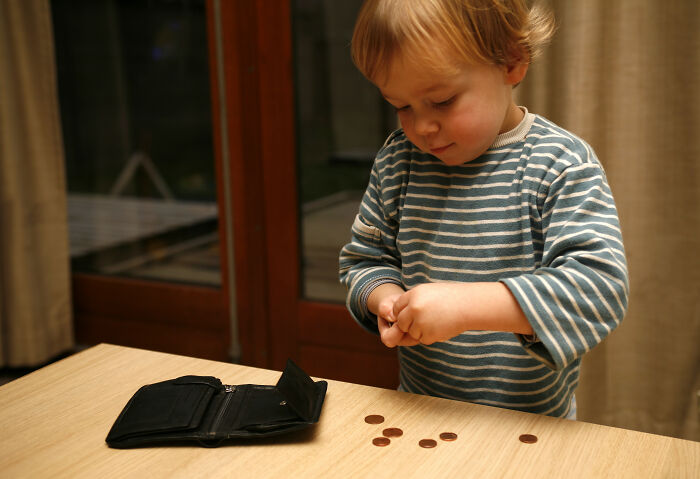 Child counting coins on a table with an open wallet nearby.