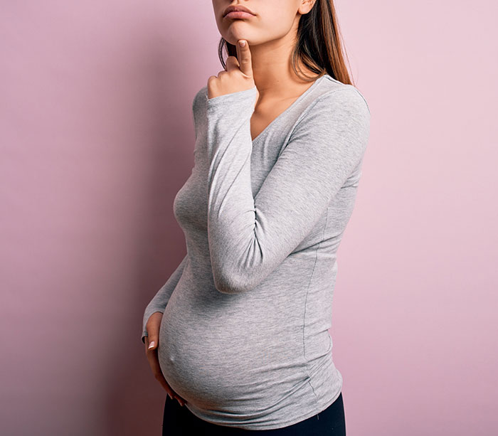 Pregnant teen in gray shirt pondering, highlighting medical mystery case.
