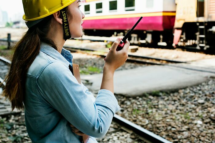 A construction worker in a safety helmet uses a walkie-talkie by train tracks, illustrating professions employing millions.
