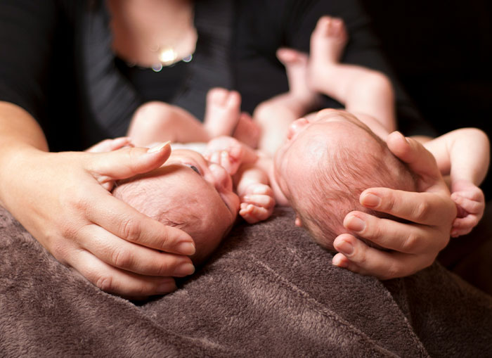 A mother cradling newborn twins, highlighting family dynamics and parenting challenges.
