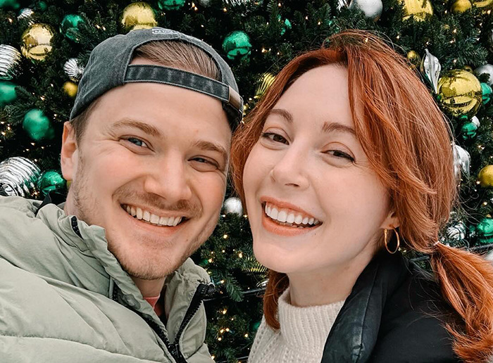 Happy couple smiling in front of a decorated Christmas tree, related to BookTube crisis. Happy couple smiling in front of a decorated Christmas tree, related to BookTube crisis.