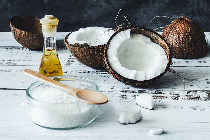 Coconut oil and shredded coconut with dark background, illustrating healthy ingredients placed on a rustic white table.