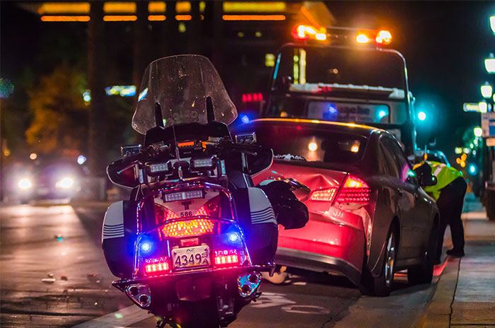 Police motorcycle at an accident scene with a tow truck under streetlights at night.