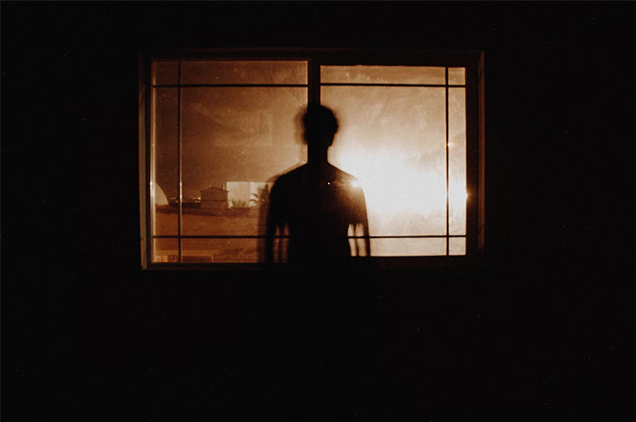 Silhouette of a person standing by a window at night, illustrating dark stories.
