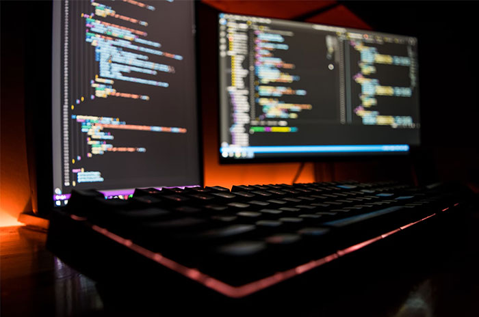 Computer screens displaying code, representing dark stories found online, with a keyboard in the foreground.