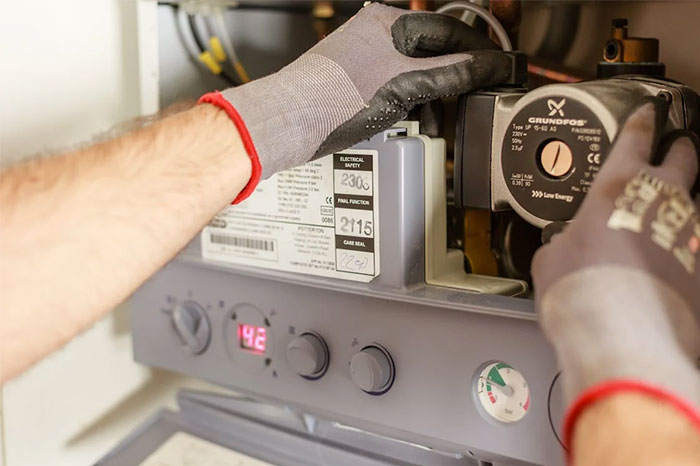 Person adjusting a boiler control panel with gloved hands, symbolizing "dark stories" maintenance and technical repair.