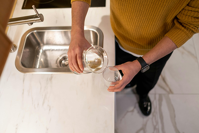 Person in a yellow sweater pouring water into a glass at a kitchen sink. Person in a yellow sweater pouring water into a glass at a kitchen sink.